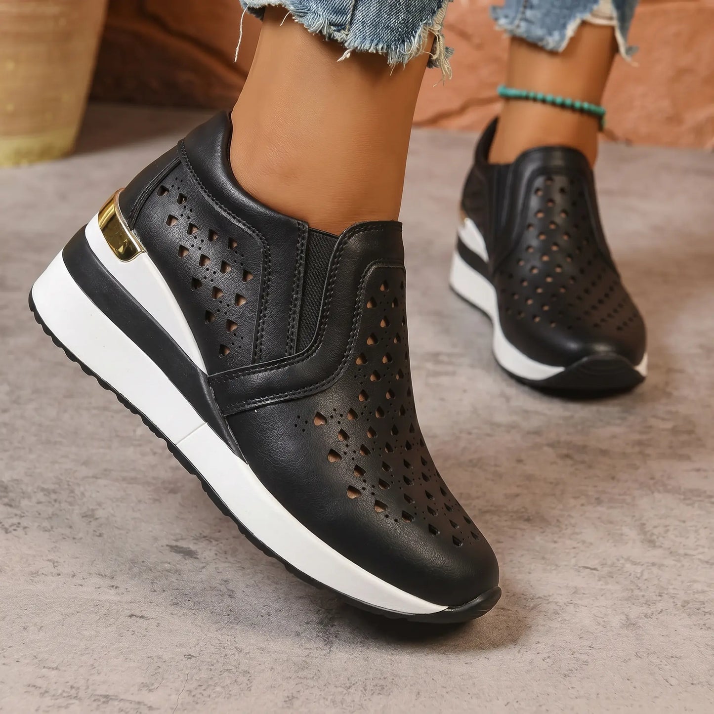 Black perforated Quorin women's wedge sneakers with a subtle heart pattern and gold heel accent, shown on a model's feet.