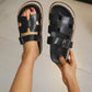 Black platform slide sandals featuring a chic H-strap design and adjustable gunmetal buckle, shown on a person's feet to highlight the chunky layered sole and comfortable fit.