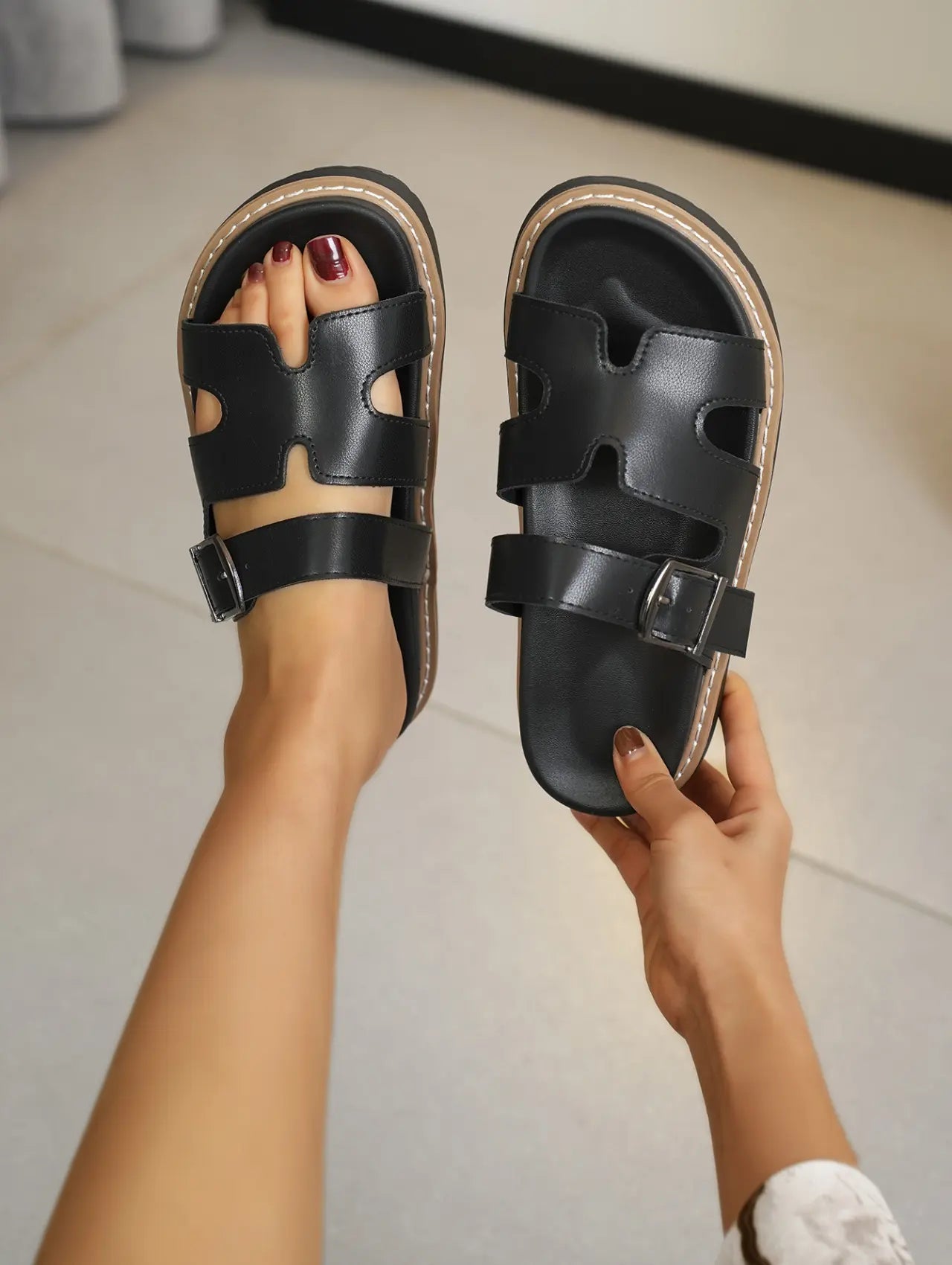 Black platform slide sandals featuring a chic H-strap design and adjustable gunmetal buckle, shown on a person's feet to highlight the chunky layered sole and comfortable fit.