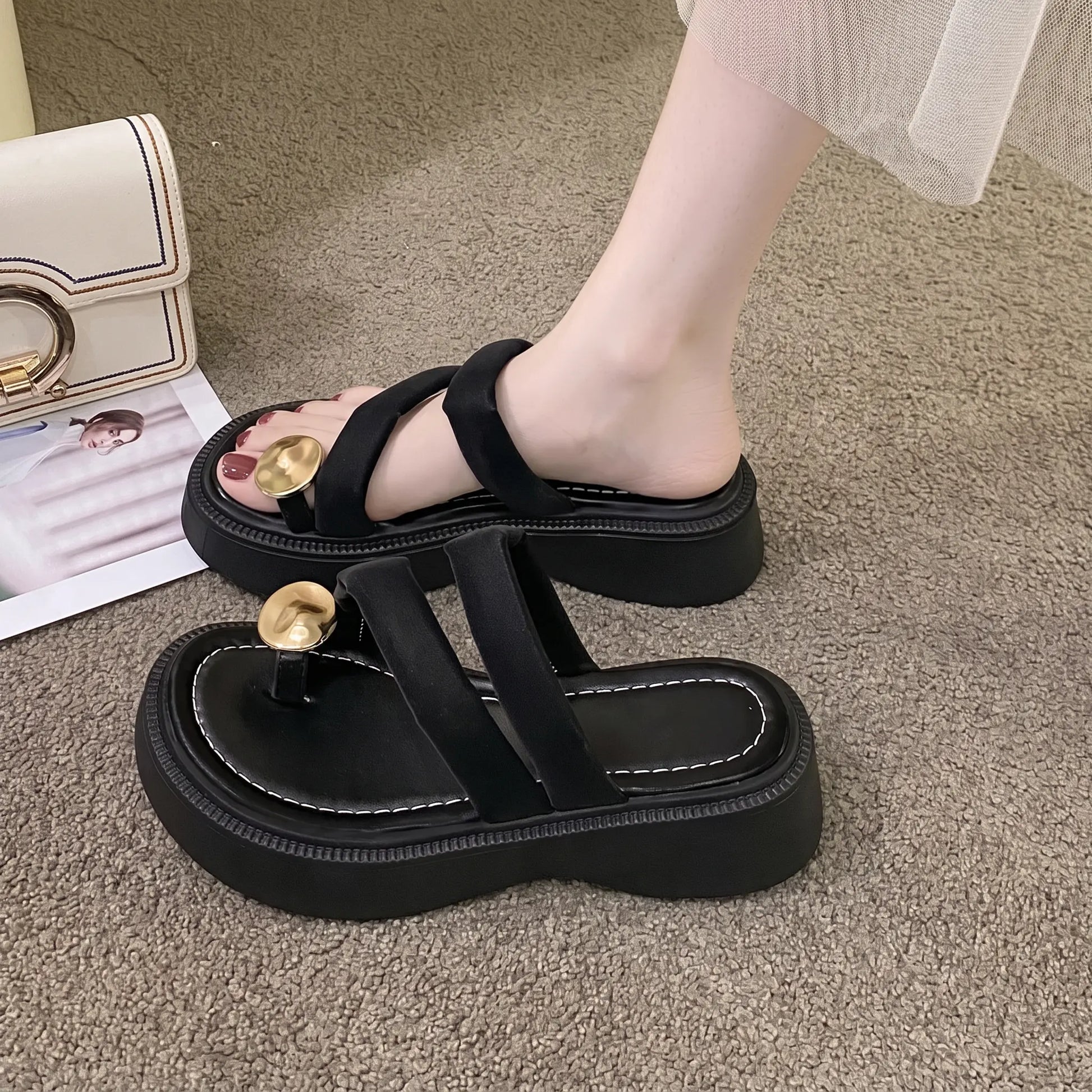 Black platform thong sandals with plush velvet-feel straps and a polished gold-tone metal buckle, shown on a foot with a cushioned footbed and chunky sole.