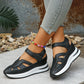 Black platform wedge sandals with cut-out straps and a white midsole, worn by a woman with jeans and a colorful anklet in a lifestyle setting.