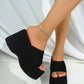 Black suede-like fabric platform wedge sandals worn by a model, showcasing the ultra-high wedge, open toe, and single strap design with a glittering anklet.