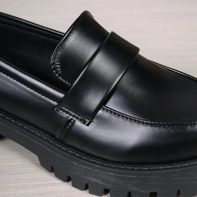Close-up of a black polished synthetic leather platform loafer, showcasing the classic penny strap detail and a chunky lug sole.