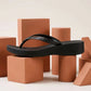 Black waterproof PVC platform wedge flip-flop, presented in a side three-quarter view, showcasing its embossed leaf straps and honeycomb textured footbed on studio props.