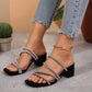 A woman's feet wearing black square-toe slide sandals adorned with sparkling rhinestone straps and a 4cm block heel, styled with distressed denim jeans.