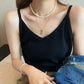 Woman modeling a black ribbed V-neck camisole with thin straps, accessorized with layered pearl necklaces, gold pendant, and denim jacket.
