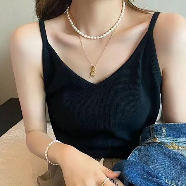 Woman modeling a black ribbed V-neck camisole with thin straps, accessorized with layered pearl necklaces, gold pendant, and denim jacket.