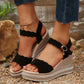 Women's black suede-like wedge sandals featuring scalloped straps, a gold buckle with a crystal charm, and a rhinestone-trimmed beige platform wedge.