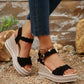 Women's black suede-like wedge sandals with scalloped straps and rhinestone-trimmed platform, worn on feet with denim jeans.