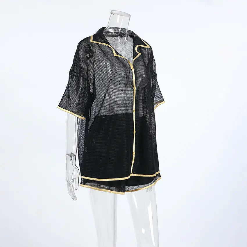 Black sheer mesh lounge set featuring a short-sleeved camp collar shirt and drawstring shorts, detailed with gold contrast piping, displayed on a mannequin against a white studio background.
