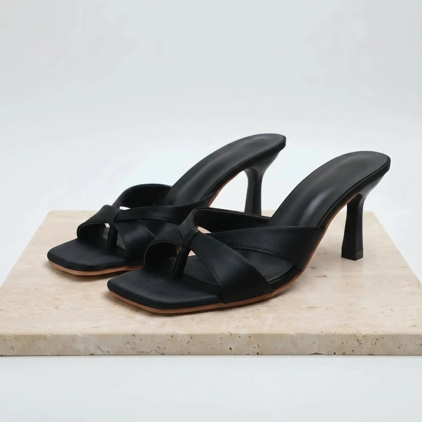 Black PU square toe stiletto mules with a knot detail across the vamp, shown from a three-quarter angle on a marble display.