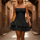 Model in a black strapless smocked mini dress with tiered eyelet ruffle skirt and scalloped hem, walking in a sunlit alleyway.