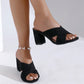 Black suede-like cross-strap block heel mules shown on a model's feet, highlighting the open toe and stable 7cm heel on a clean studio background.