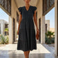 Model in black Torvun ruffled tiered midi dress with V-neck and flutter sleeves, walking through an elegant architectural hallway.