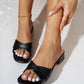 Black slip-on slide sandals for women featuring a modern square toe and chic twisted strap vamp, shown on feet with white-pedicured toes and a gold ankle bracelet.