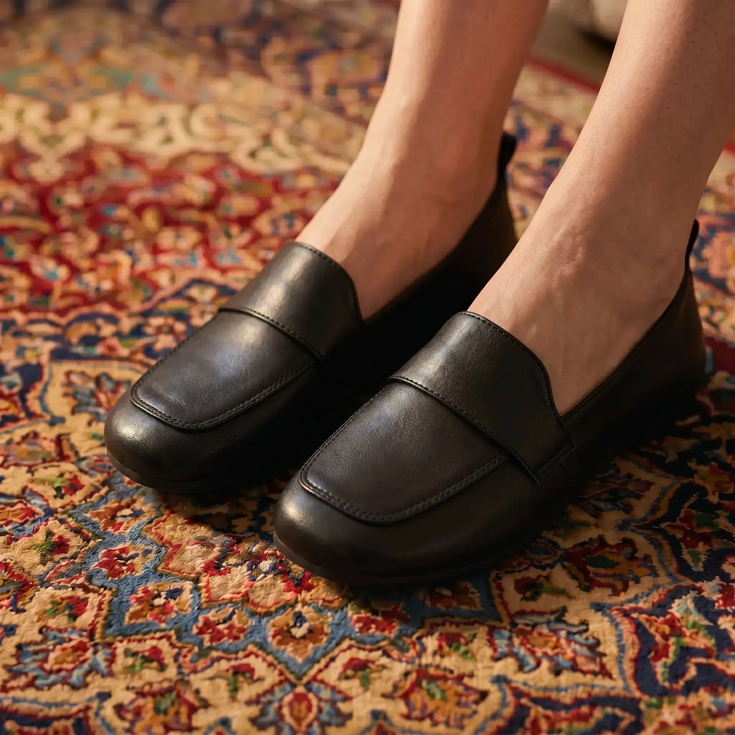 Elegant Midnight Black vegan leather slip-on loafers, featuring a rounded toe and transverse strap, worn on a colorful patterned rug.