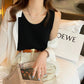 Elegant black waffle knit sleeveless camisole with a scoop neck, worn by a model. The relaxed fit top is layered under a white button-down shirt and styled with light trousers, a brown belt, and a delicate pearl necklace, showcasing its versatile appeal.