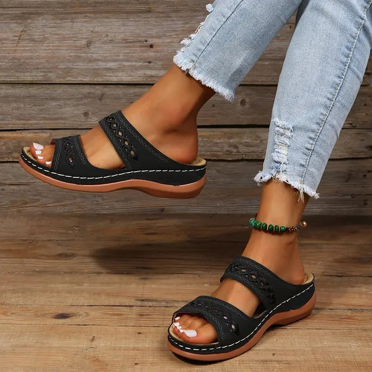 Close-up of black bohemian-chic wedge sandals with geometric embroidered straps, worn on a woman's feet with light blue jeans.