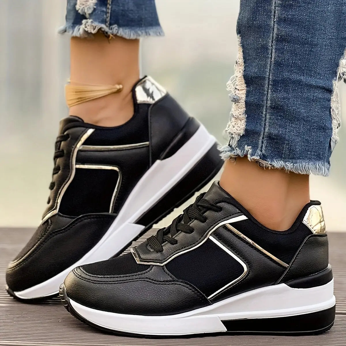 Black low-top wedge sneakers with subtle rose gold metallic accents and a layered white and grey sole, worn with distressed denim jeans.