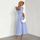Sleeveless light blue midi dress with gathered halter neckline and side waist cut-outs, worn by a model holding a white handbag, presented against a studio background.