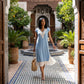 Woman wearing a Zethri light blue knit midi dress with white floral lace V-neck and pleated underlay, walking through an ornate Moorish courtyard.