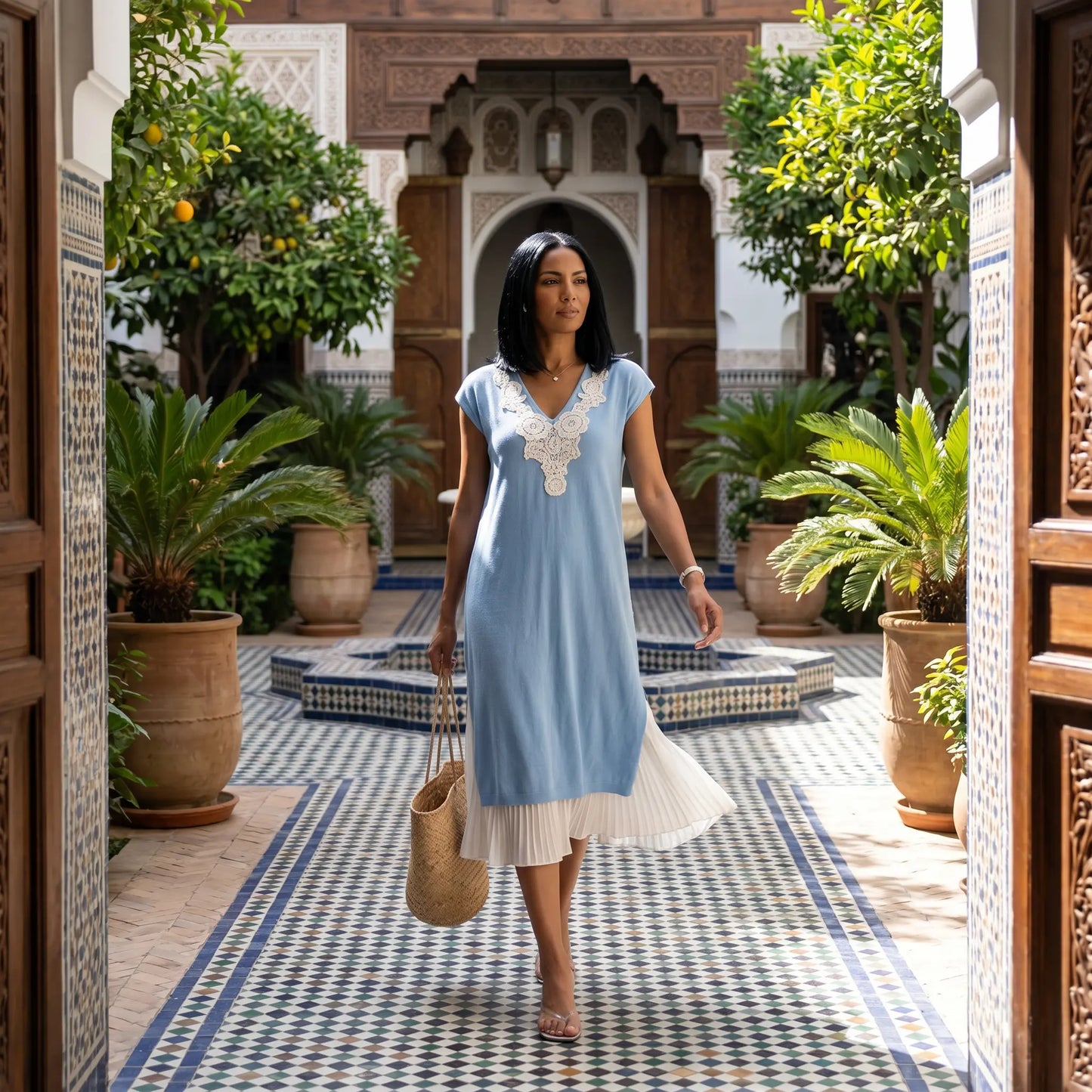 Woman wearing a Zethri light blue knit midi dress with white floral lace V-neck and pleated underlay, walking through an ornate Moorish courtyard.
