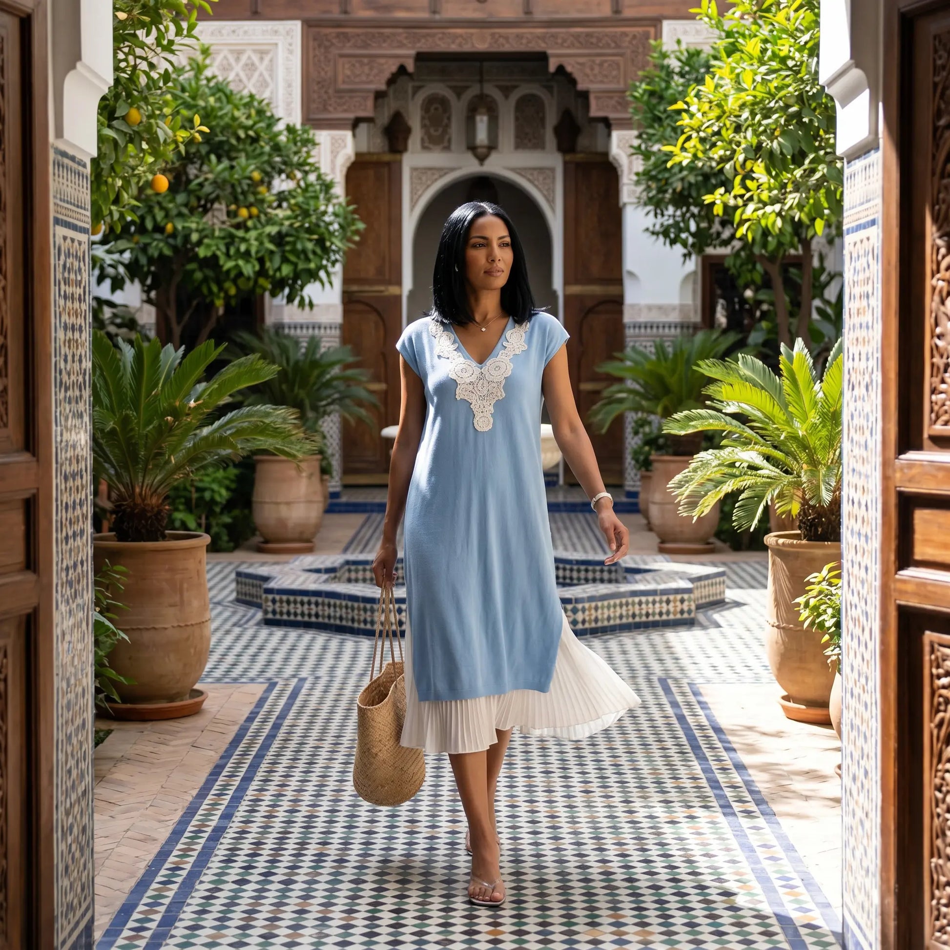 Woman wearing a Zethri light blue knit midi dress with white floral lace V-neck and pleated underlay, walking through an ornate Moorish courtyard.