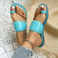 Close-up of feet wearing blue patent toe-thong flat sandals with a braided strap detail, paired with ripped jeans and a gold ankle bracelet.