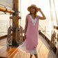 Blush Pink Zethri knit midi dress, featuring a V-neck white floral lace appliqué and pleated hem, worn by a woman on a boat at sunset.