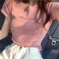 A woman wears a Tenzai slim-fit blush pink jersey t-shirt with embroidered "MISCHIEF" lettering on the chest, showcasing its elegant silhouette in a casual setting.