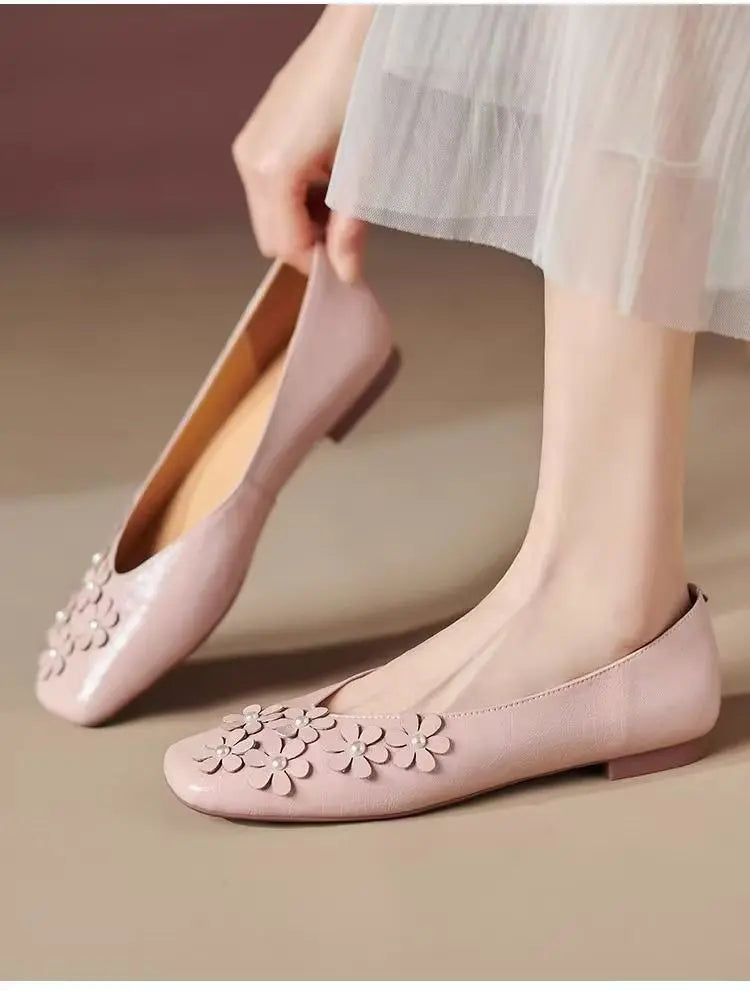 Elegant Blush Rose floral square-toe flats with intricate tonal appliques and pearl centers, worn on a foot with a hand adjusting a second shoe.