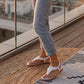 Woman wearing white bohemian flat t-strap sandals with 3D floral appliques and elastic slingback, standing on a rooftop terrace at sunset.