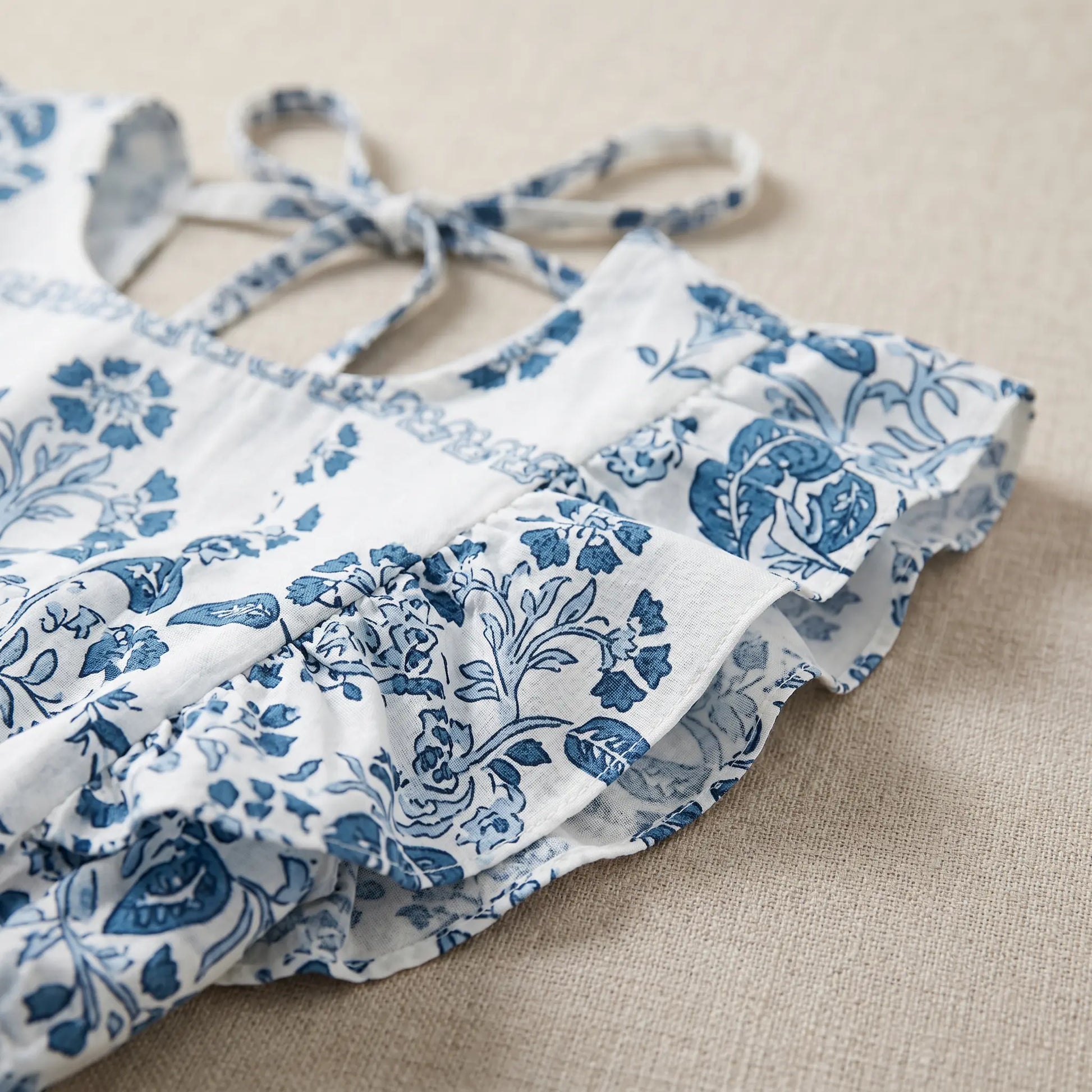Close-up of a white bohemian midi dress featuring a blue floral print, delicate ruffled cap sleeves, and a tie closure for the open back.