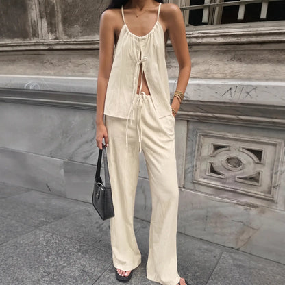 Woman wearing an oatmeal beige bohemian linen-blend halter top with a tie-front and flowy wide-leg trousers, styled in an urban setting. Elegant summer outfit.