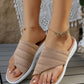 Model's feet wearing beige woven thong sandals with intricate geometric diamond pattern, set on a light wooden deck with boho-inspired decor.
