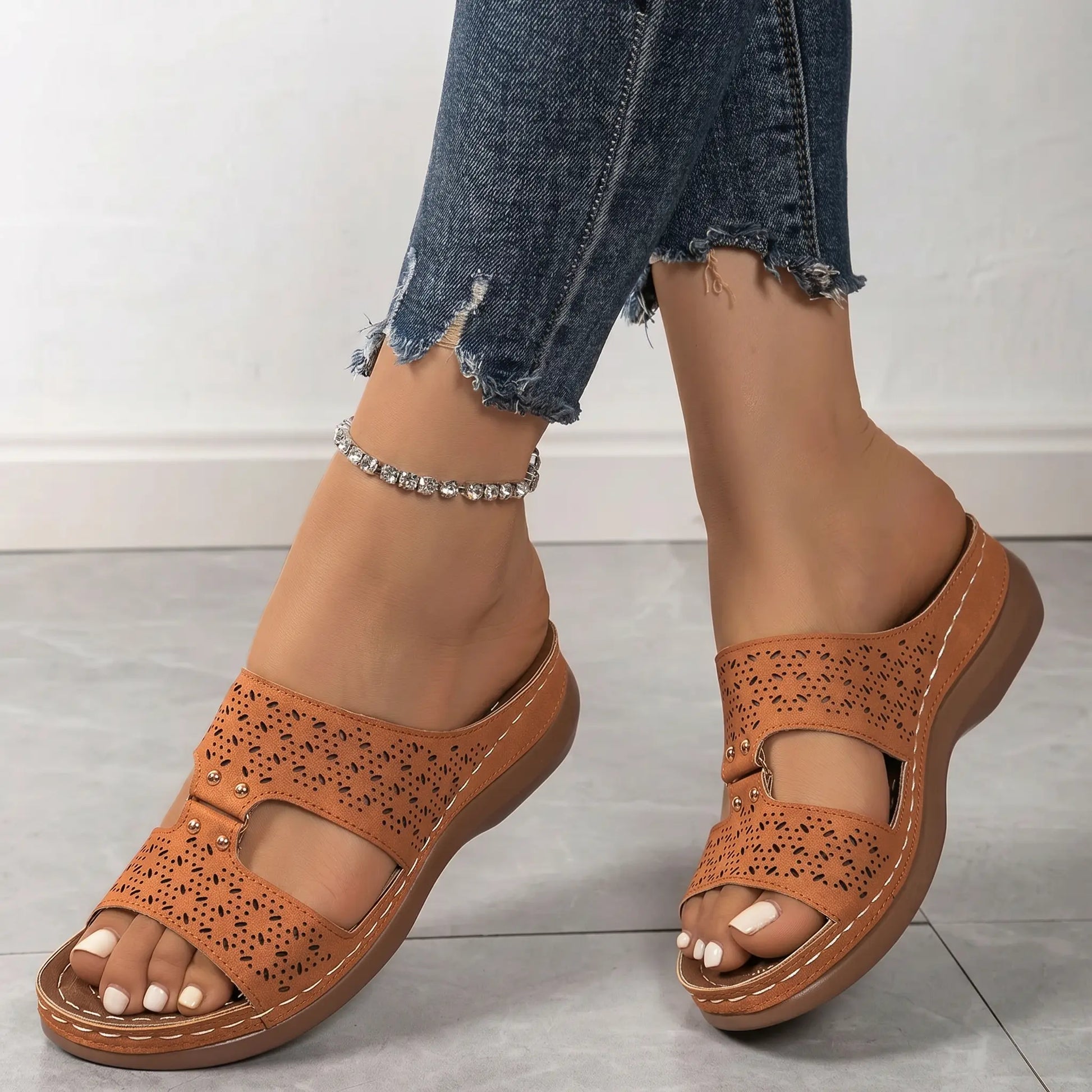 Briska women's beige laser-cut wedge sandals styled with ripped denim jeans and a sparkling anklet, showcasing comfort and bohemian chic. Side view.