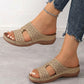 Close-up of beige Briska laser-cut wedge slip-on sandals worn by a woman with blue jeans, showcasing the intricate geometric pattern and contoured comfort sole.