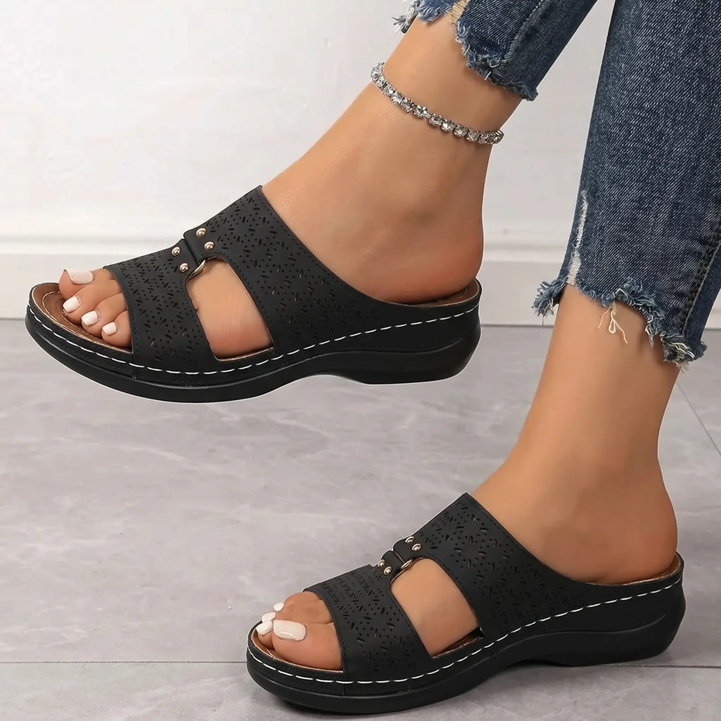 Briska black laser-cut slip-on sandals with a low wedge heel and metallic stud details, styled with ripped jeans.