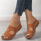 Woman's feet wearing tan Briska laser-cut slip-on wedge sandals with distressed blue jeans and a silver anklet, showcasing intricate detailing and comfort.
