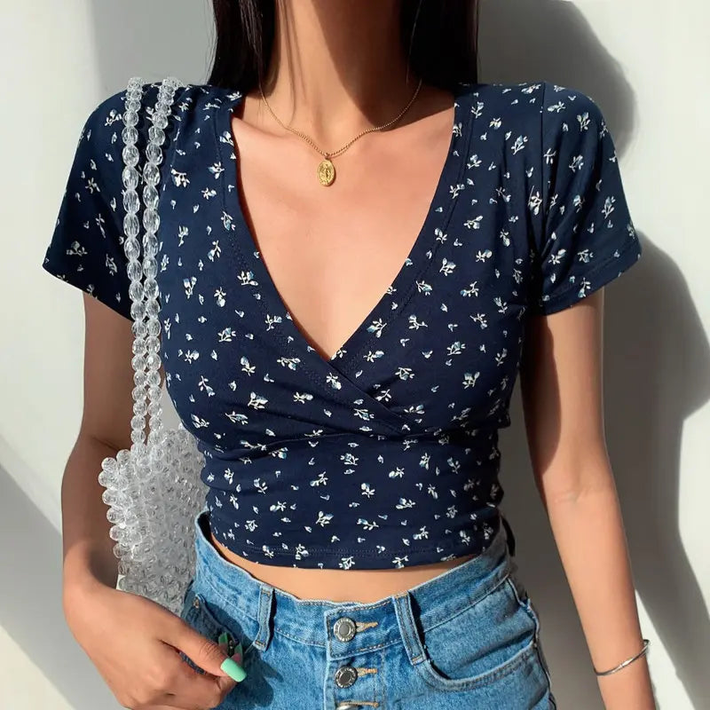 Model wearing Brivan navy blue floral V-neck crop top, front view. Highlights faux-wrap design, short cap sleeves, and delicate white and blue print.