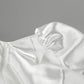 Close-up of a white satin blouse showing ruffled detailing at the collar and smocked elastic gathering on the voluminous trumpet sleeve cuff.