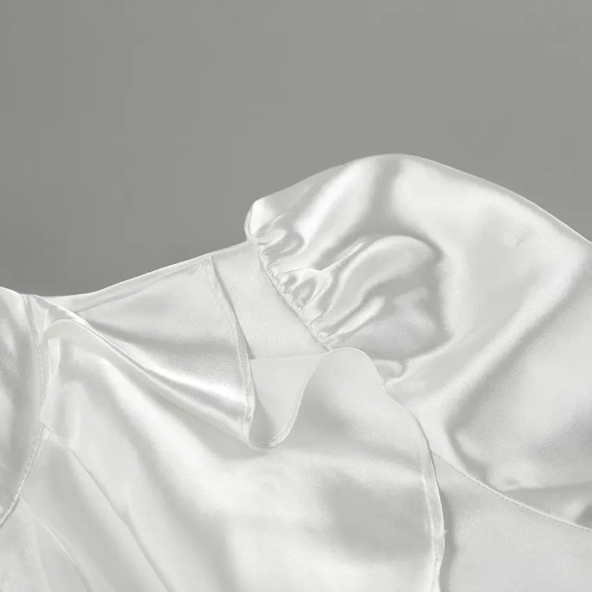 Close-up of a white satin blouse showing ruffled detailing at the collar and smocked elastic gathering on the voluminous trumpet sleeve cuff.