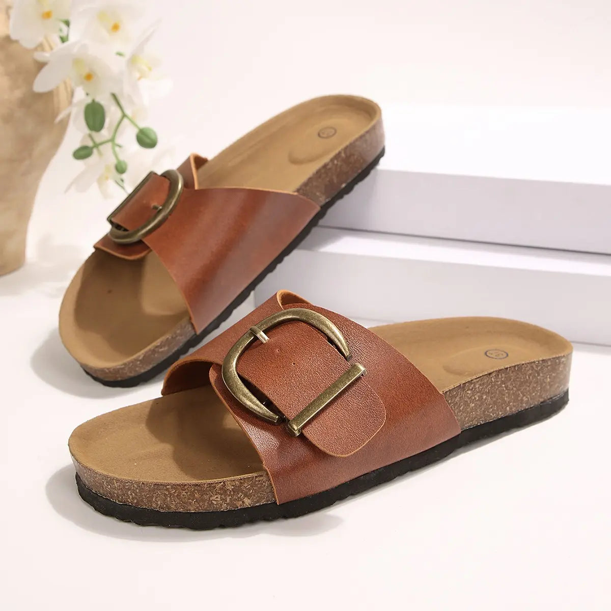 Brown PU leather slip-on slide sandals featuring an antique brass buckle and a contoured natural cork footbed, displayed as a pair.