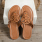 Brown embellished flat thong sandals with ornate circular cut-out vamp and gold stud accents, displayed on a wooden surface.