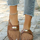 Women's brown mesh pointed-toe flat mules with a faux leather strap and polished gold oval hardware, styled with distressed denim jeans on a paved outdoor surface.