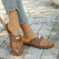 Brown mesh pointed-toe flat mules worn by a model with distressed denim jeans and a gold anklet, showcasing the intricate diamond weave and gold oval hardware detail on a stone patio.