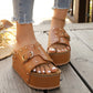 Brown studded platform slide sandals with gold buckles, shown on feet wearing distressed denim on a wooden deck.