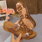 Brown women's platform slide sandals featuring textured interlocking straps, gold-tone hardware, and a contoured cork-effect sole, shown on a model's foot with a decorative floral accent in the background.