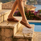 Woman wearing Kozwen brown waterproof platform wedge flip-flops with braided straps, descending sunlit stone steps with water splashing.