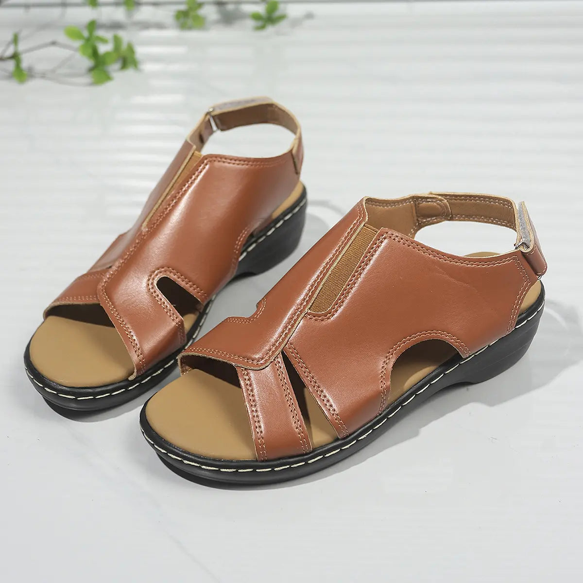 Pair of elegant brown faux leather peep-toe wedge sandals with white contrast stitching and adjustable ankle straps, shown from a three-quarter angle.